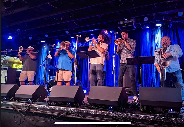 5 piece brass band performs on stage.